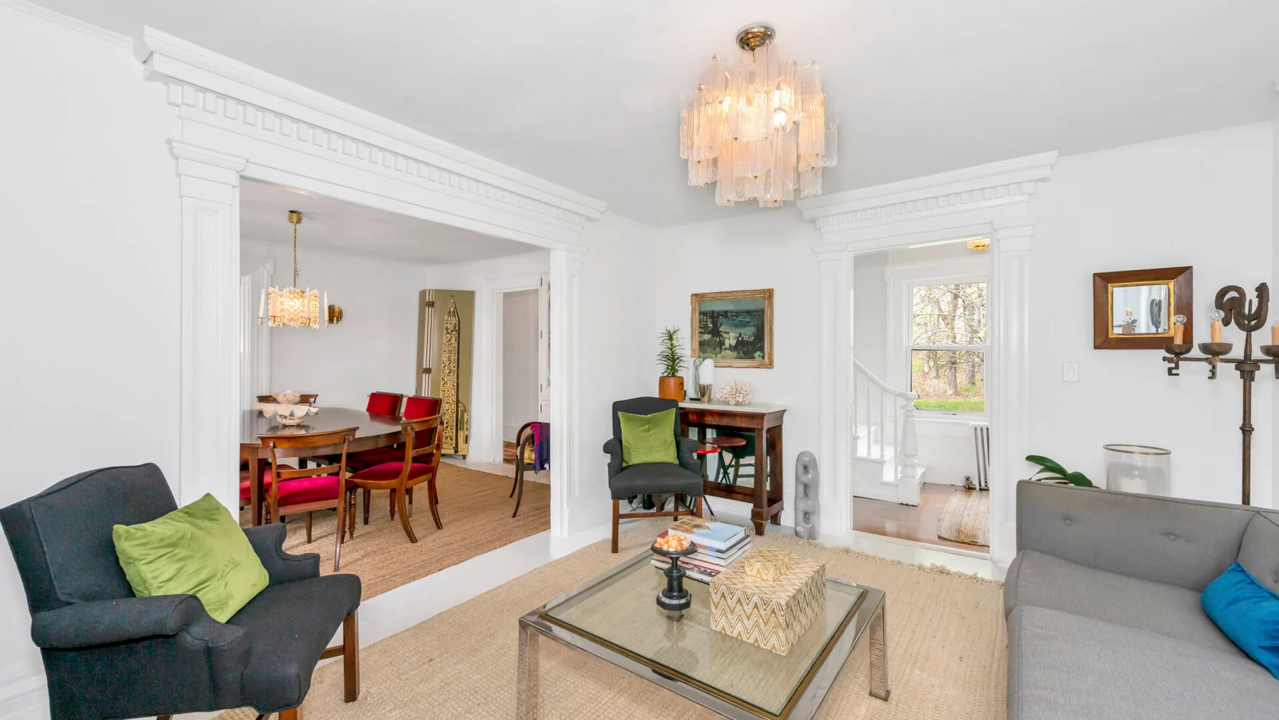 A bright living room with seating, a glass coffee table, and an adjoining dining area.