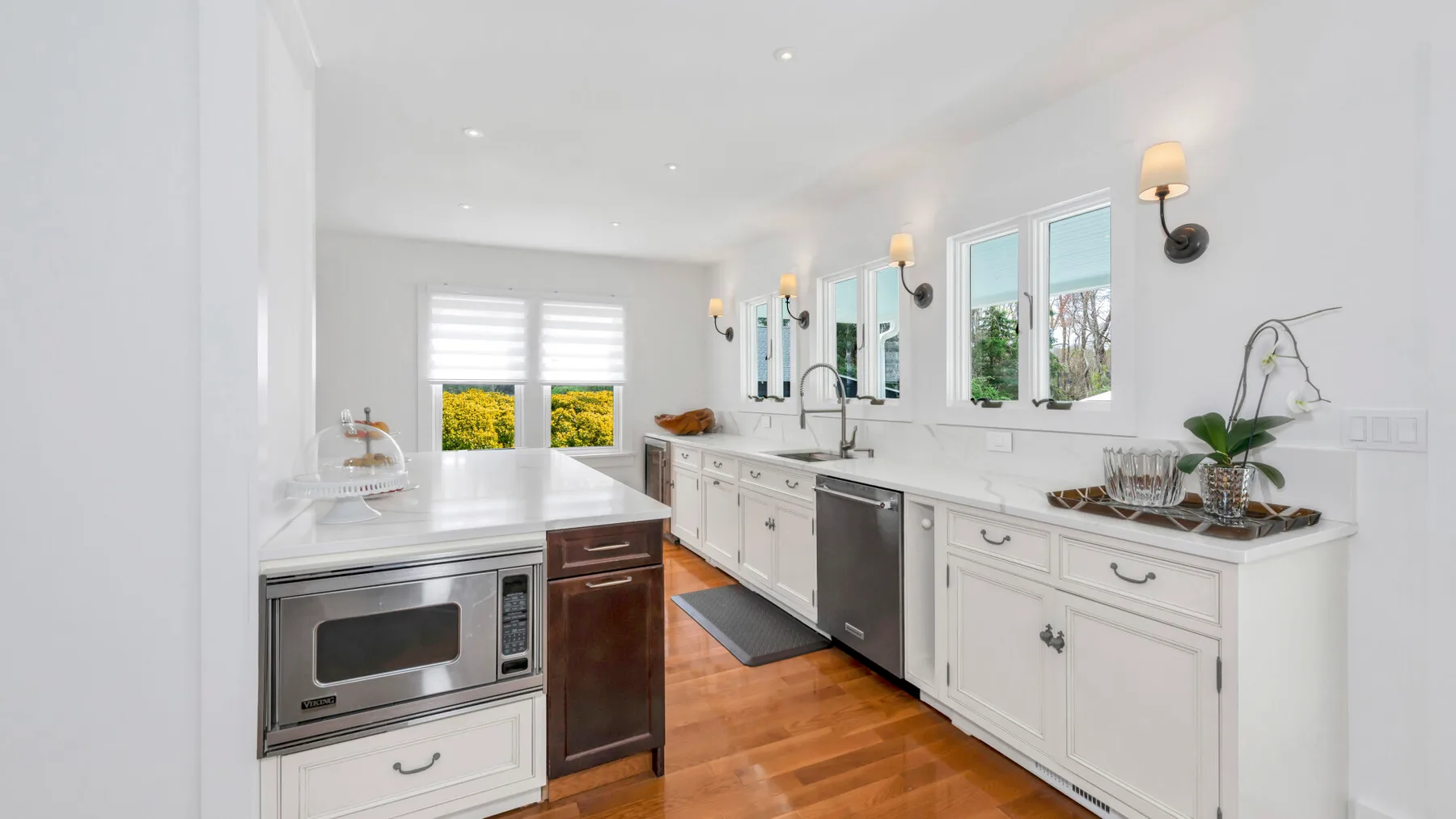 A bright kitchen with white cabinetry, stainless steel appliances, and a long countertop.