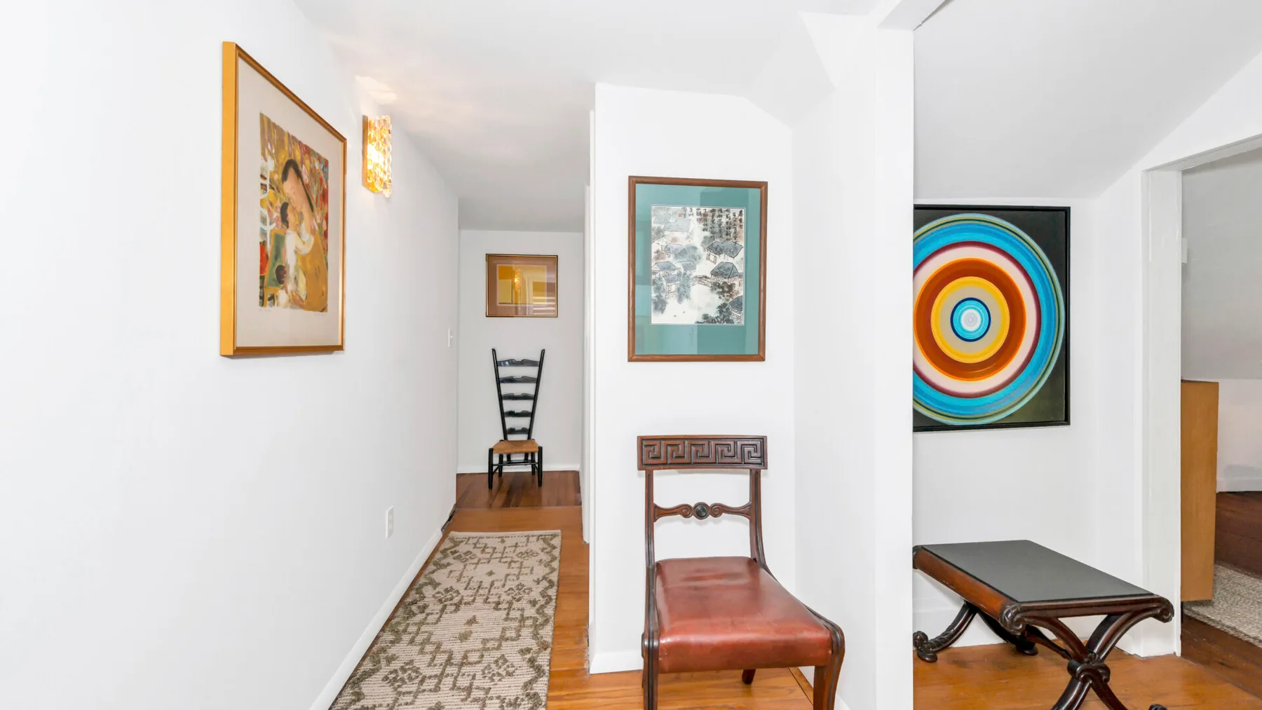 A bright hallway with framed artwork and wooden seating.