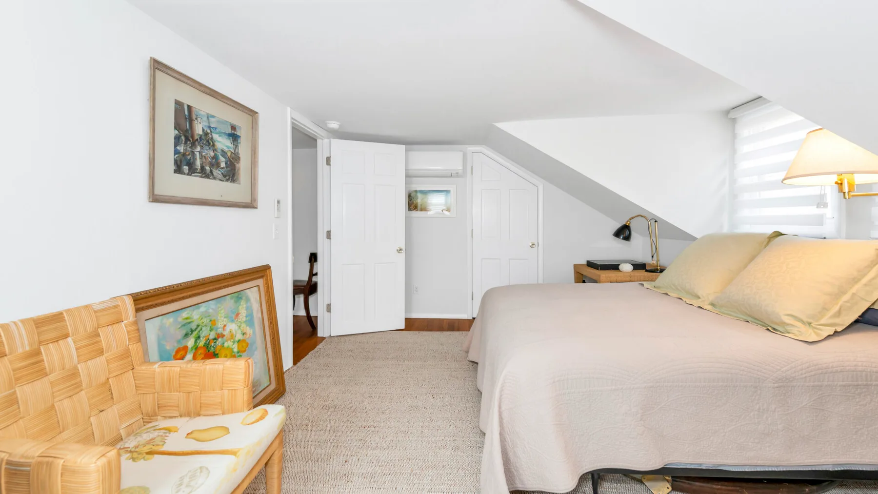 A bedroom with a bed beneath a sloped ceiling and a woven chair.