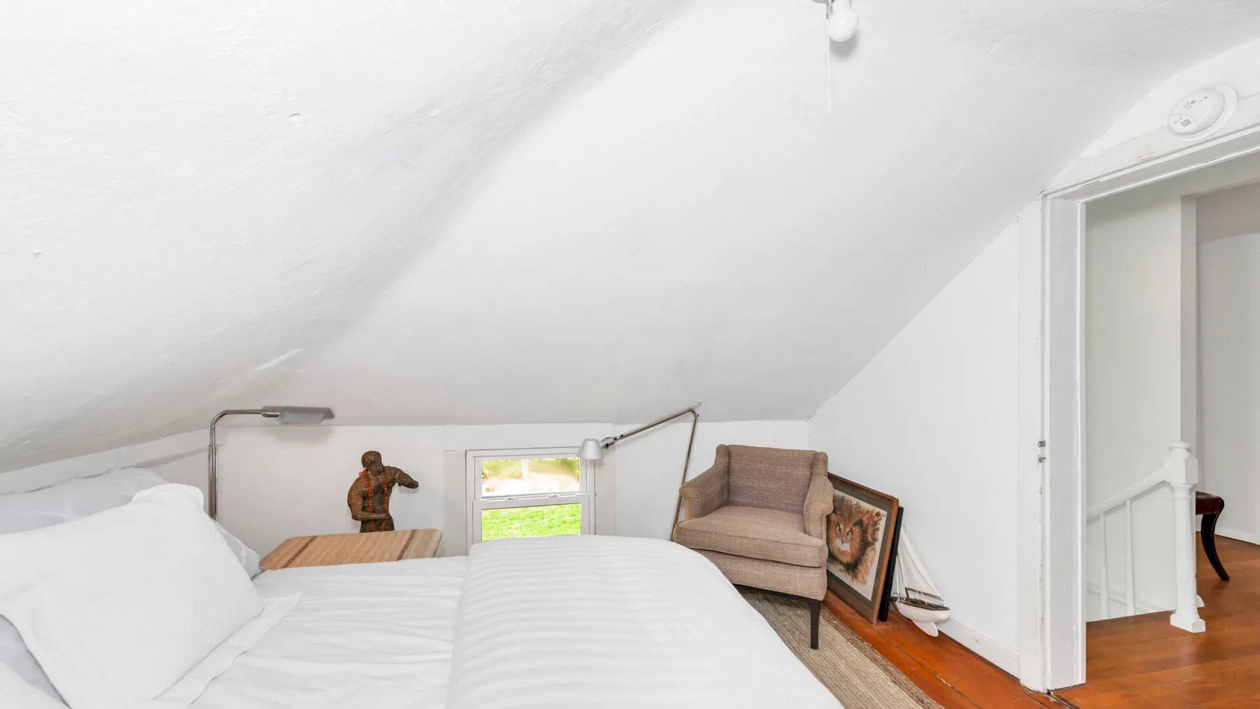 A bright attic bedroom with a bed beneath a sloped ceiling.