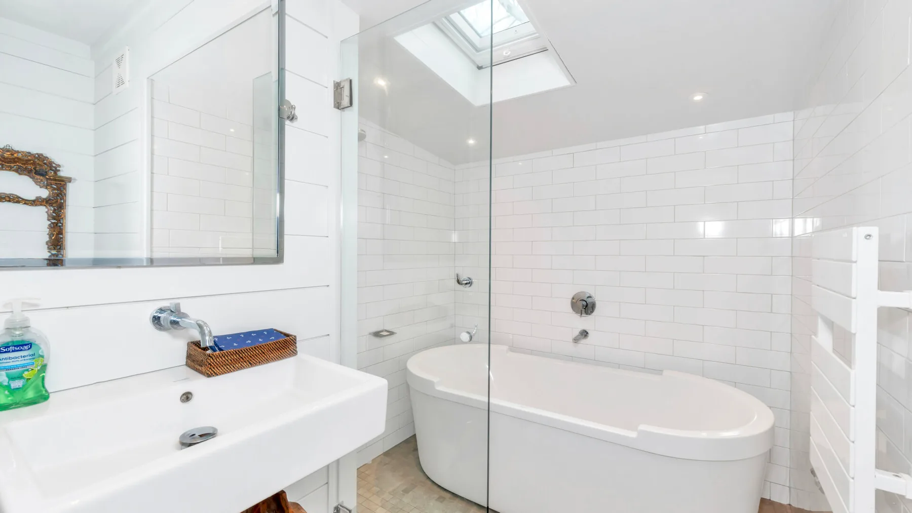 A bright bathroom with a bathtub, glass shower screen, and sink.