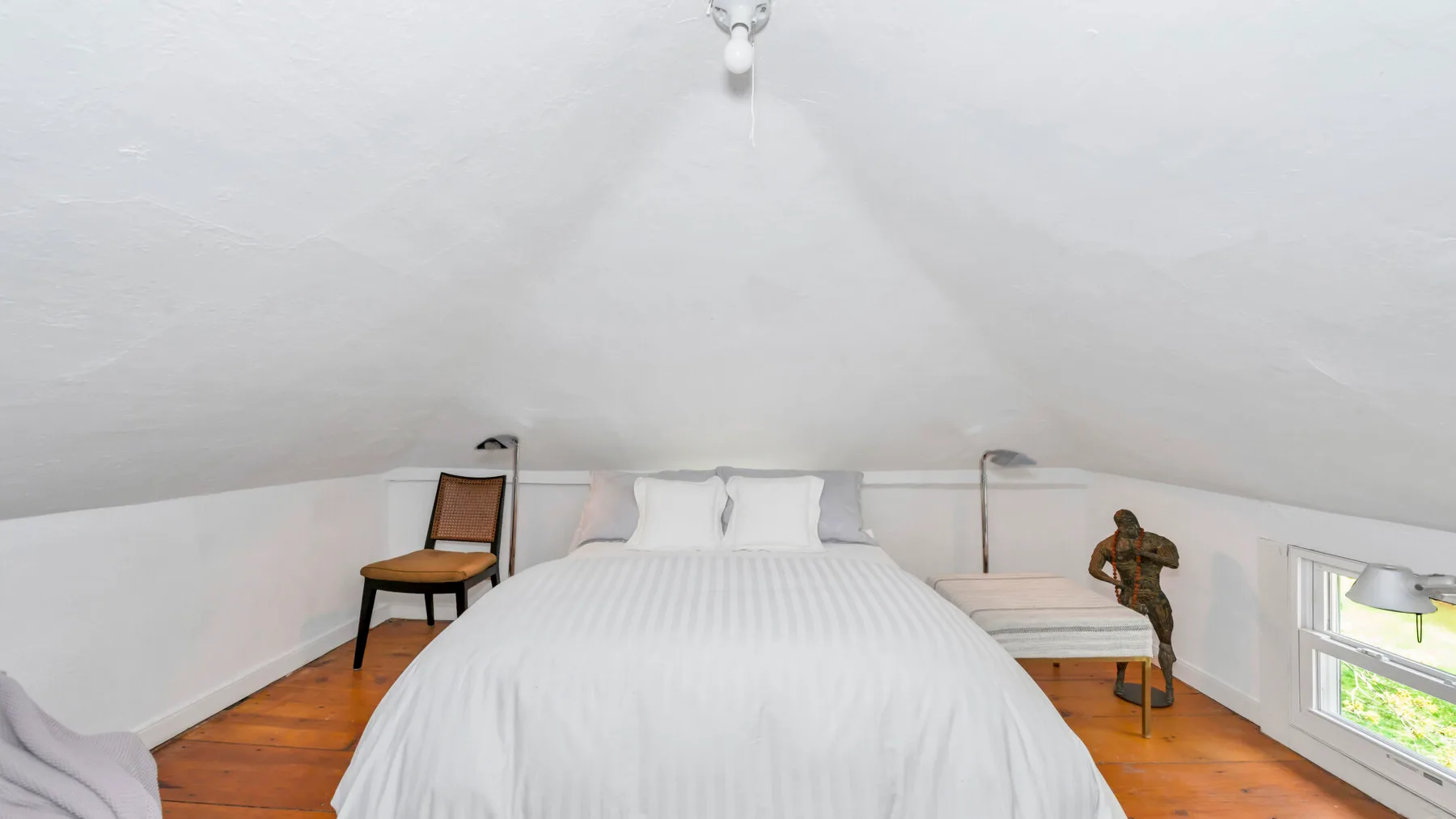 A bedroom with a bed beneath a sloped ceiling and wooden flooring.