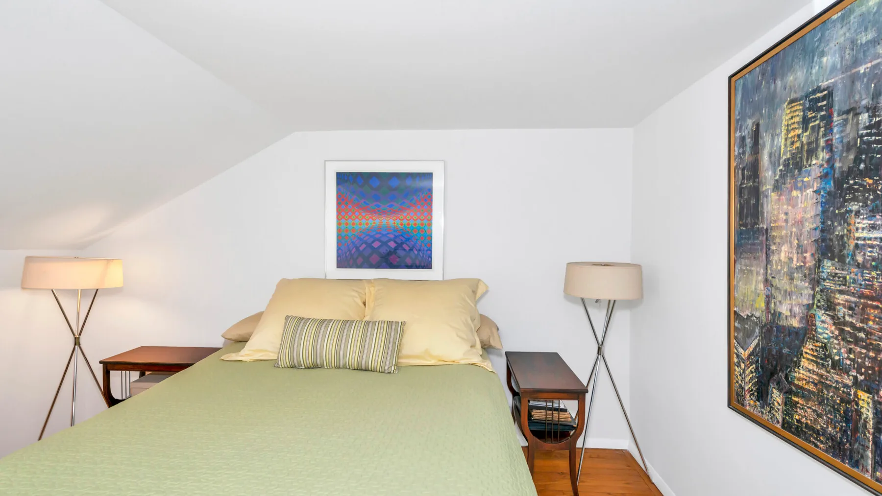 A bedroom with a bed, bedside tables, lamps, and framed artwork.