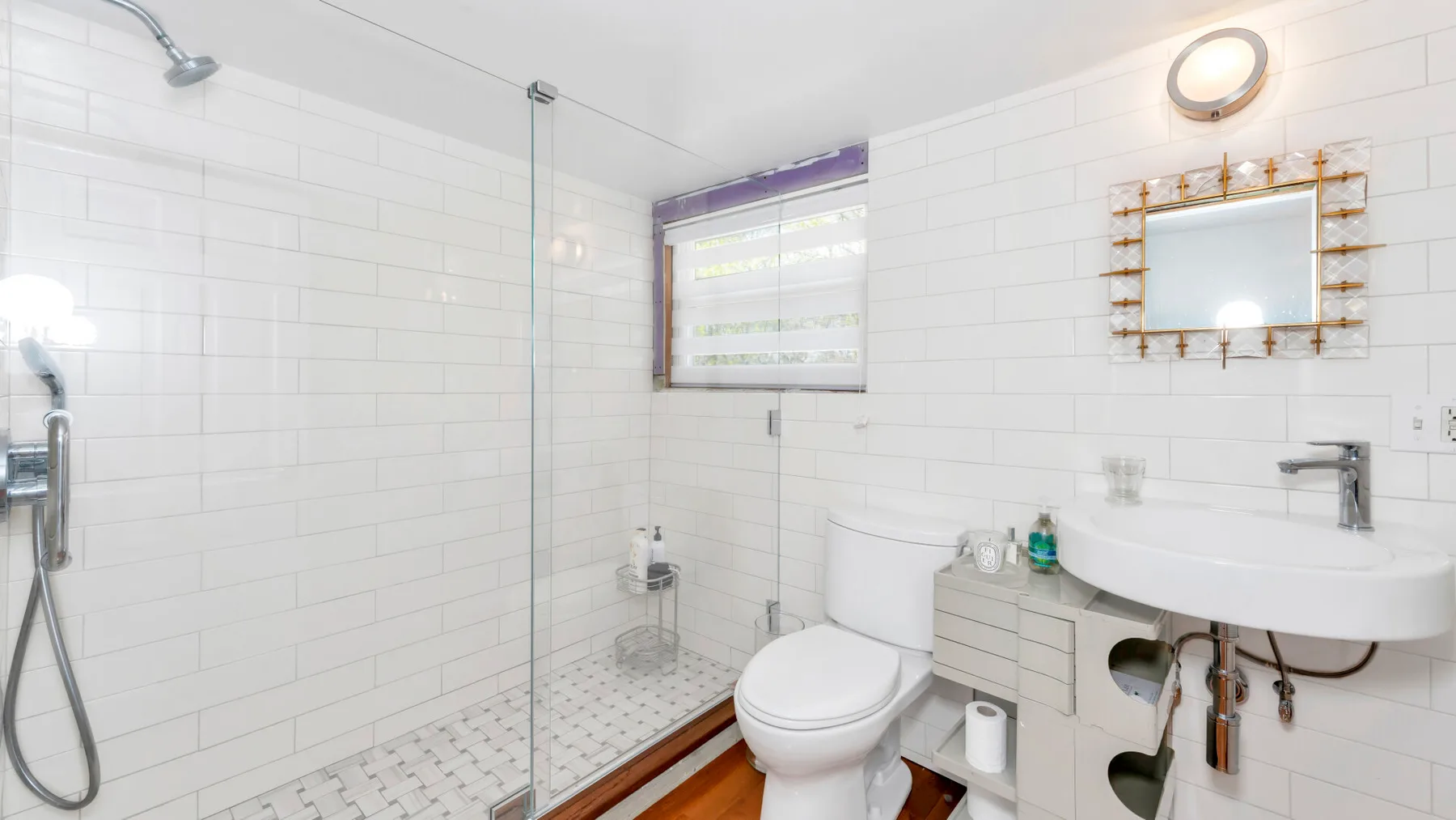 A bright tiled bathroom with a shower, toilet, and wall-mounted sink.