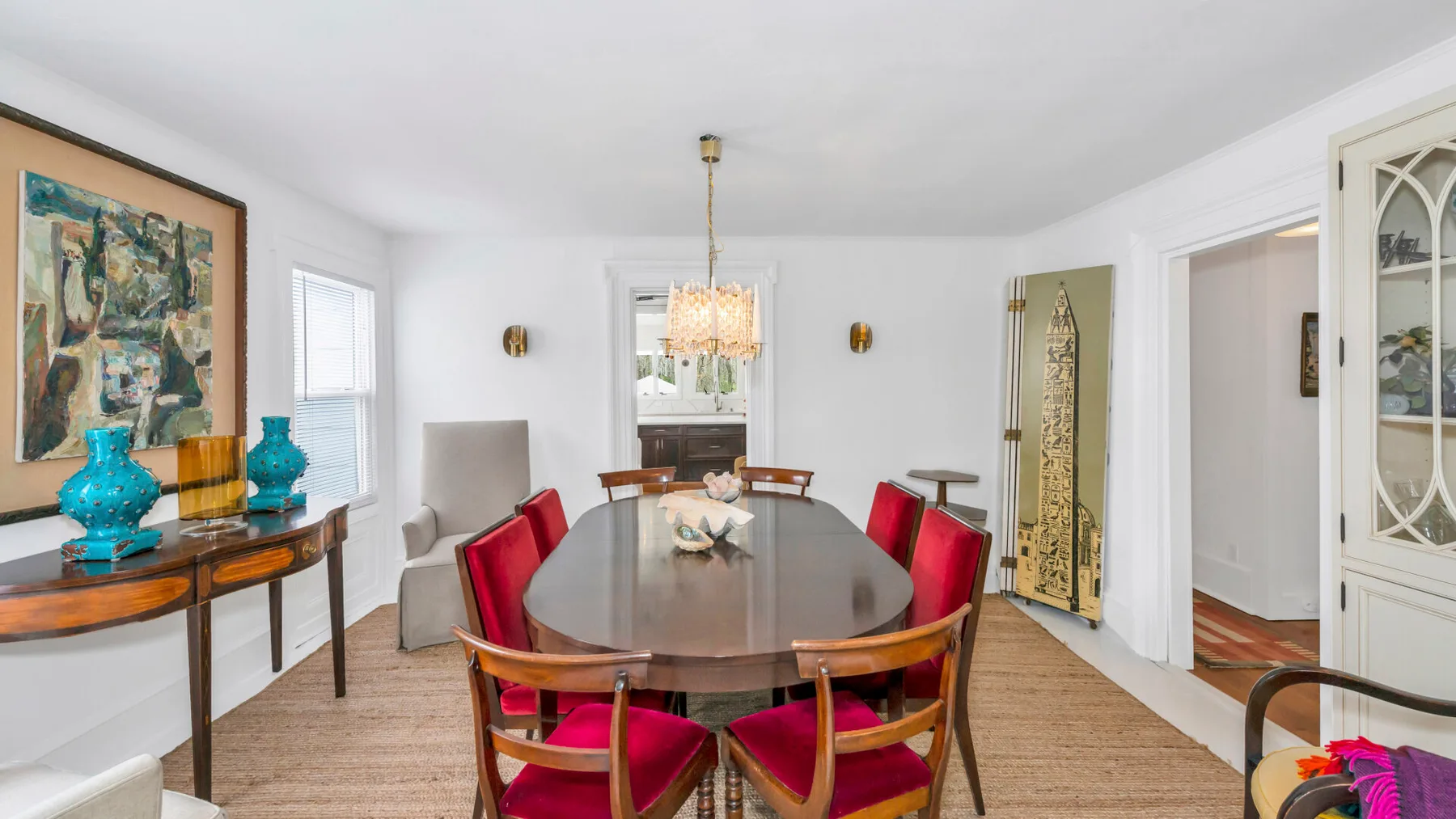A bright dining room with a long table and red upholstered seating.