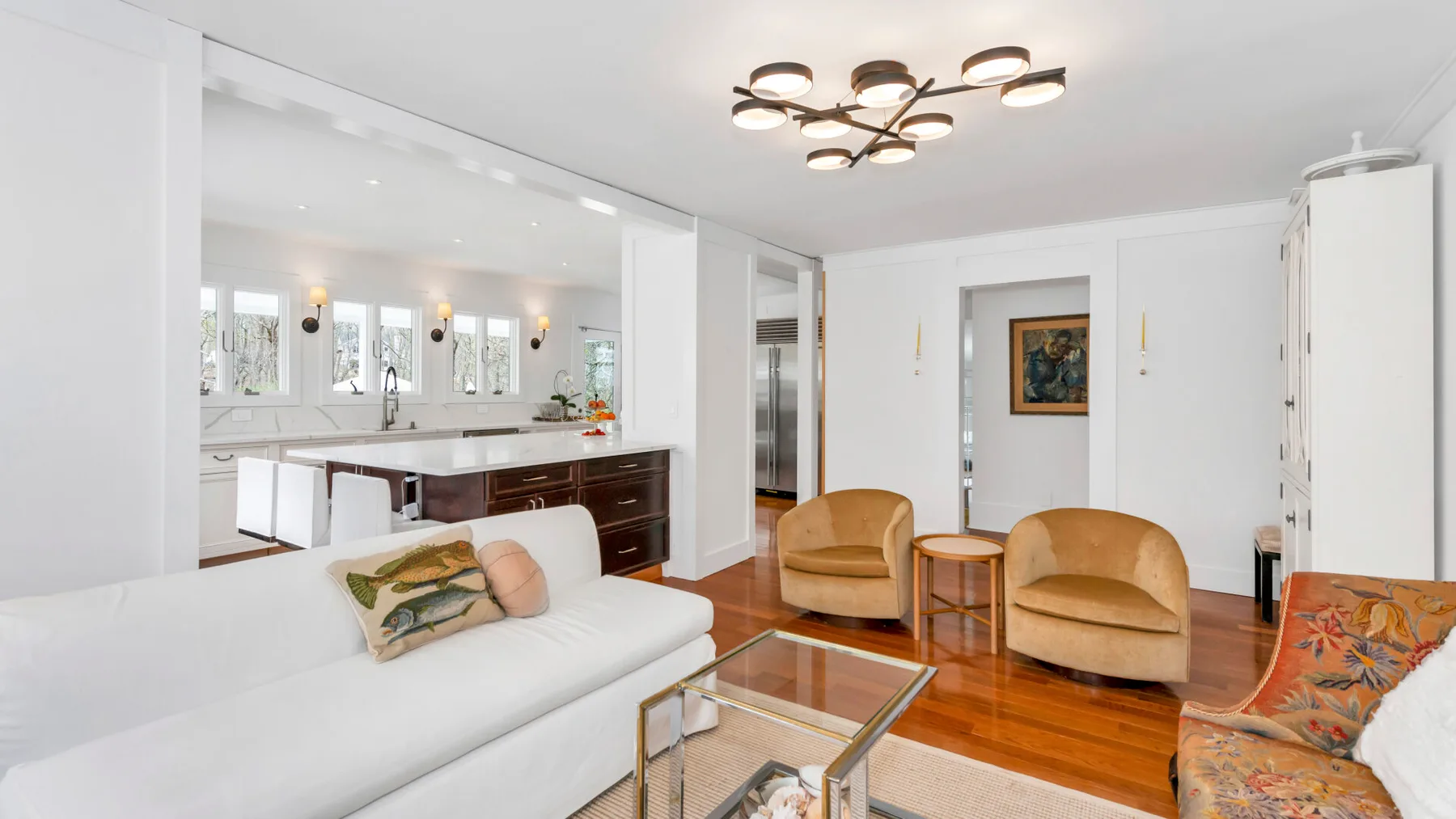 A bright living room opens onto a kitchen, with seating around a glass coffee table.