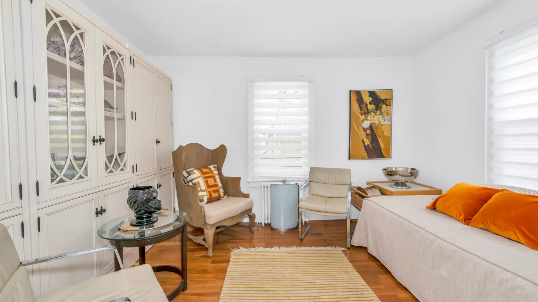A bright living room with seating, a striped rug, and a large white cabinet.