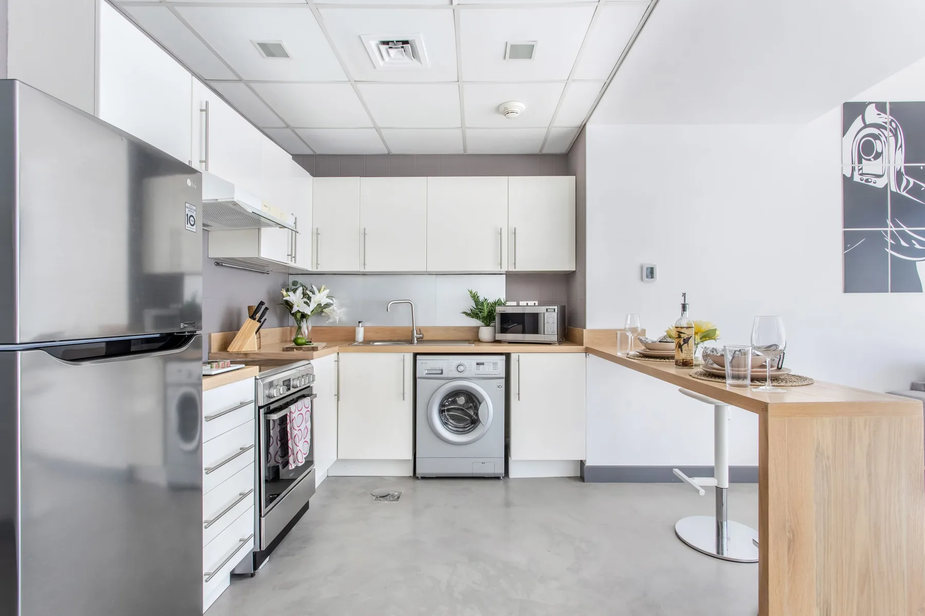 Una cocina luminosa y moderna con armarios blancos, encimeras de madera y una lavadora.