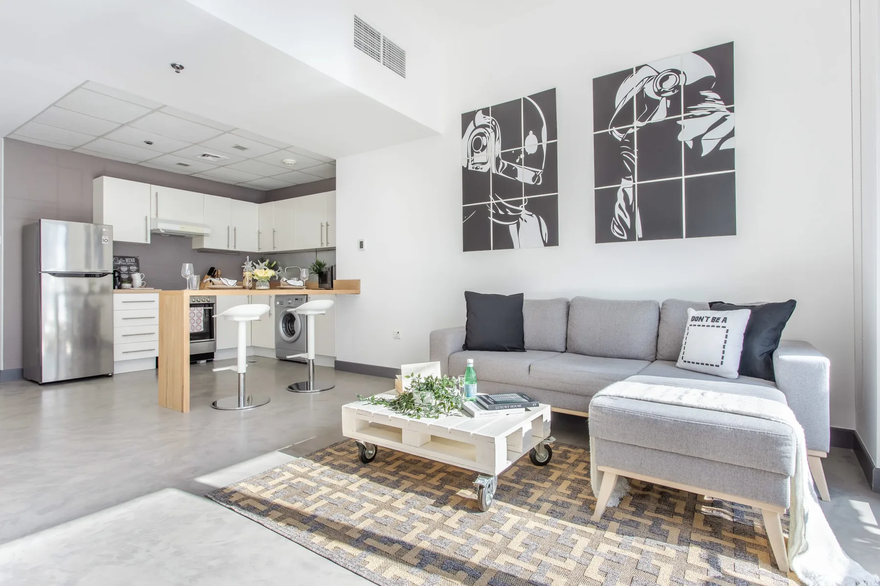 Una sala luminosa con un sofá seccional gris y una pequeña cocina contigua.