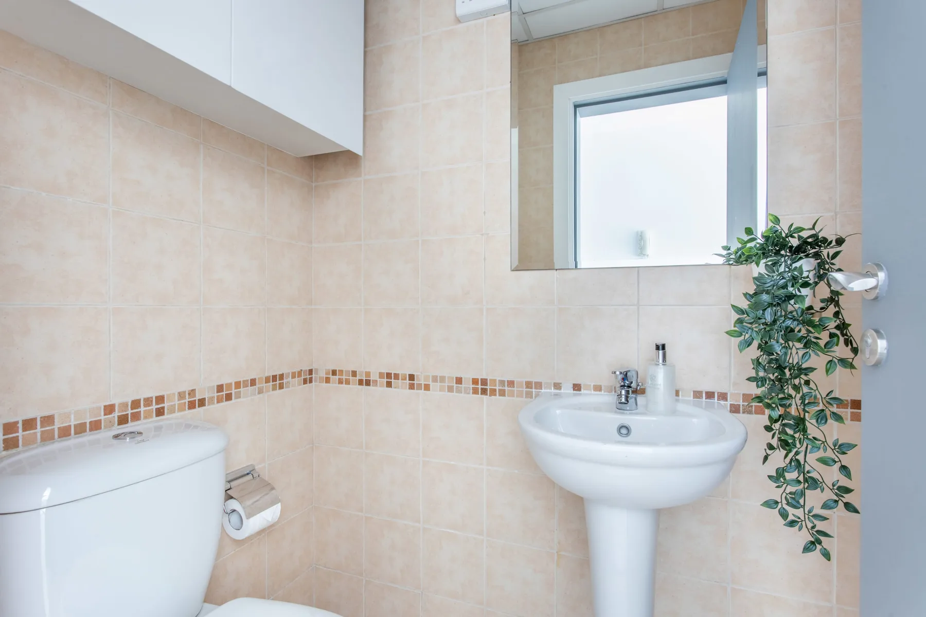 Un baño con azulejos, lavabo, inodoro y una planta frondosa.