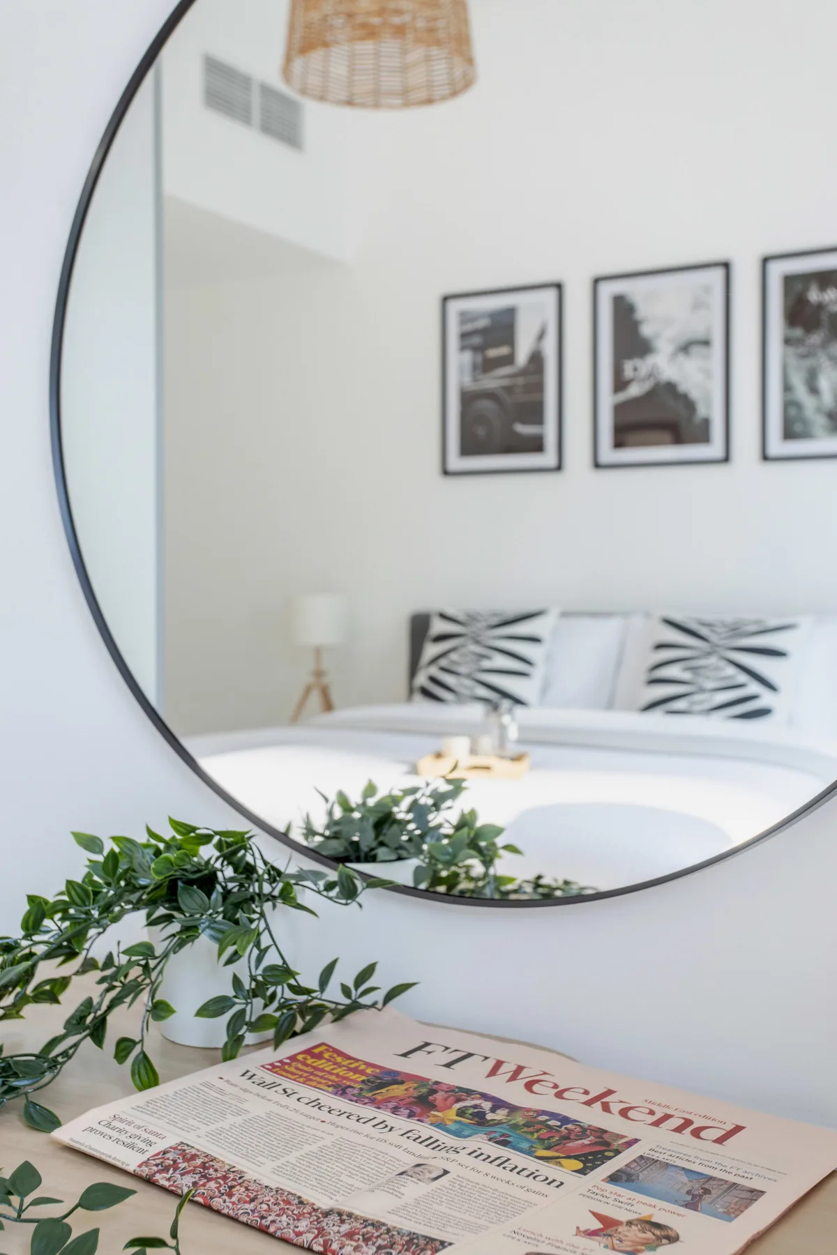 Un dormitorio reflejado en un espejo redondo, con almohadas estampadas y un periódico en primer plano.