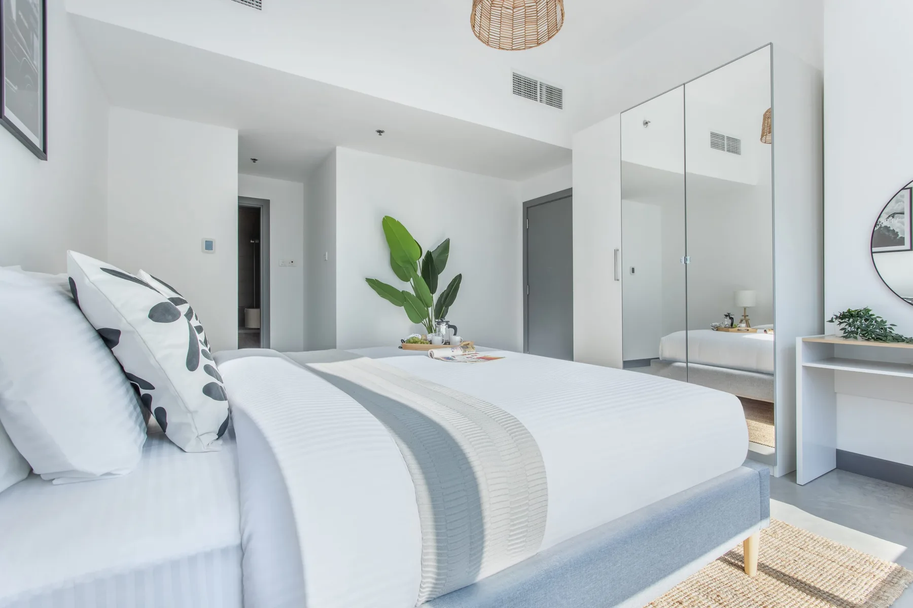 Un dormitorio luminoso con ropa de cama blanca y una planta frondosa junto a la cama.