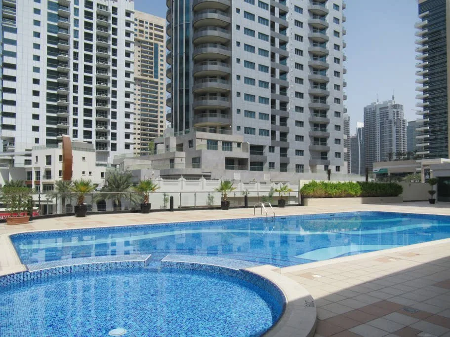 Una piscina al aire libre está junto a edificios altos y una terraza de baldosas.