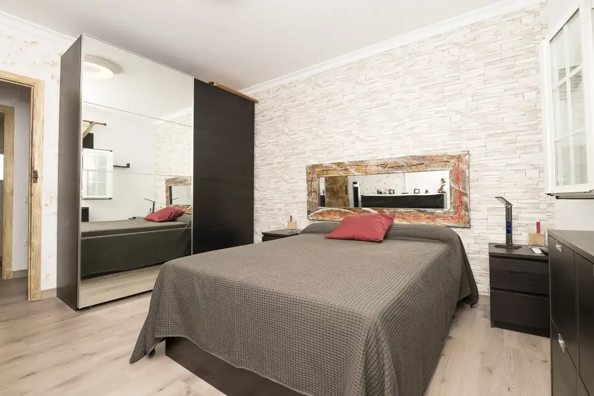 A bedroom with a bed, mirrored wardrobe, and light-colored walls.