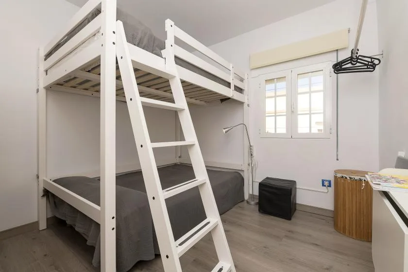 A bedroom with a white bunk bed, window, and gray bedding.