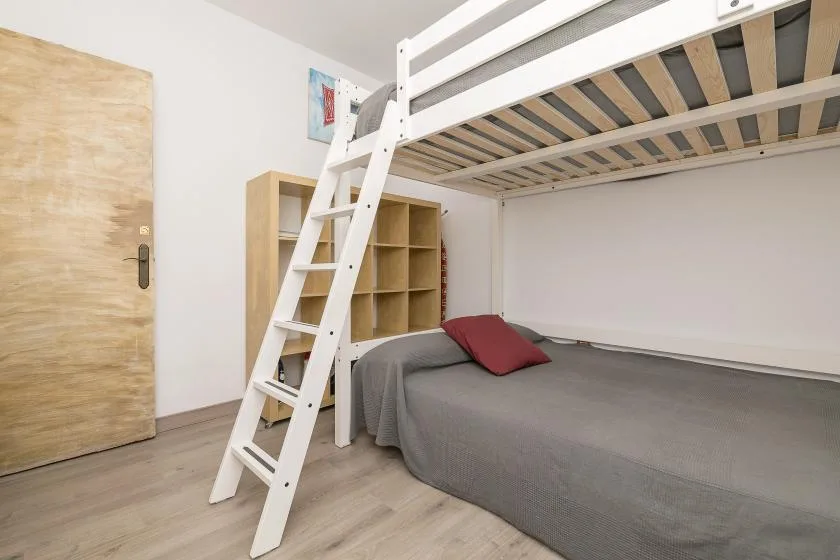 A bedroom with a gray bed beneath a white loft bed and ladder.
