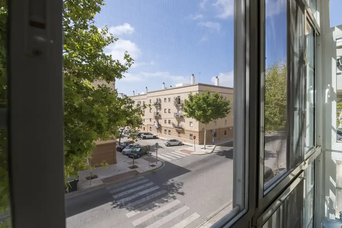 Street scene viewed through an open window, with a crosswalk and buildings opposite.