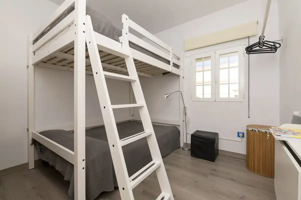 A bedroom with a white bunk bed, a window, and a small desk.
