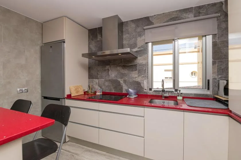 A modern kitchen with red countertops and a window above the sink.
