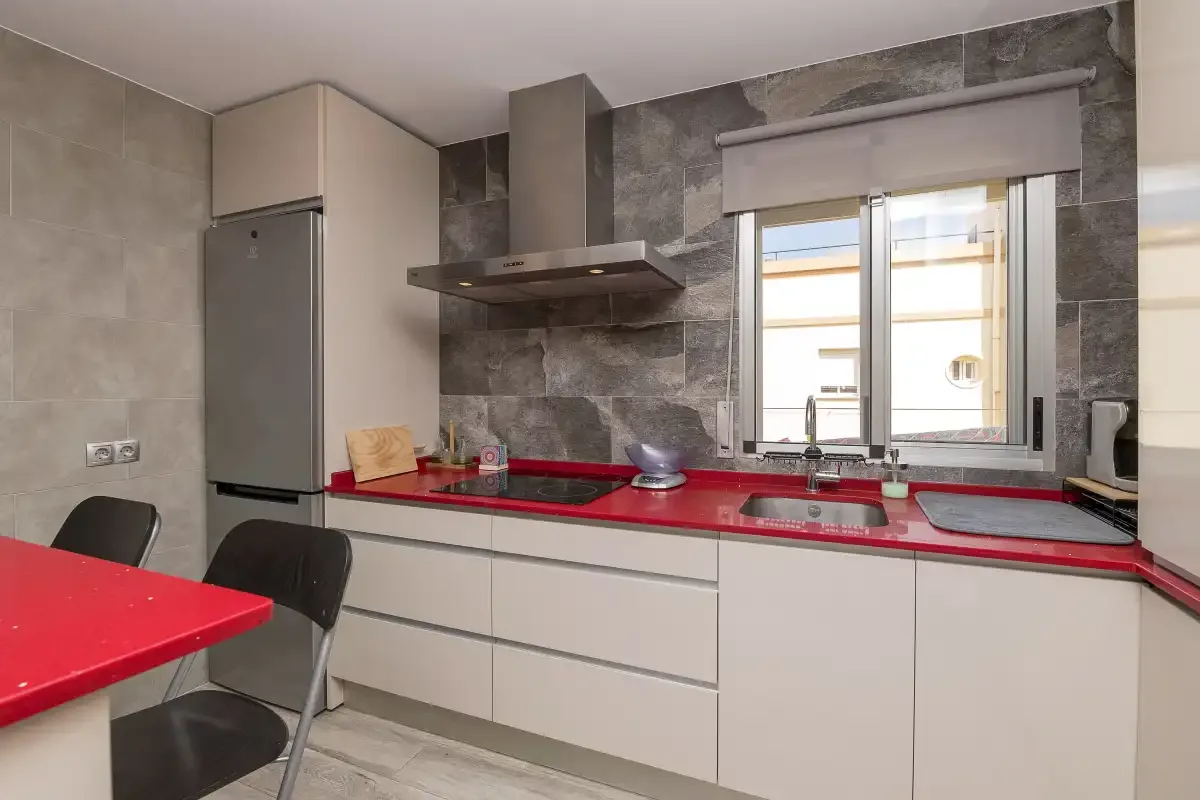 A modern kitchen with a red countertop and a window above the sink.