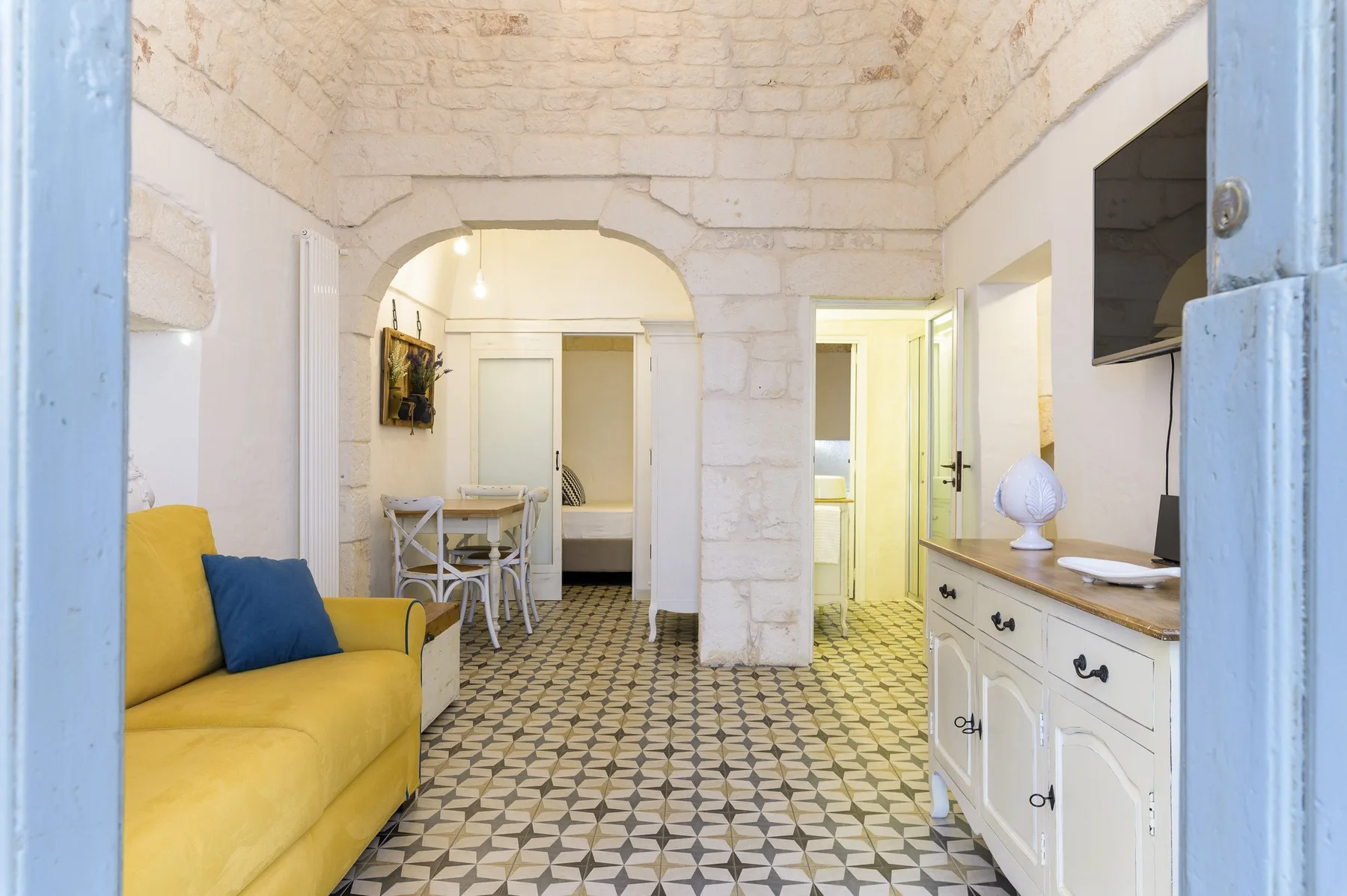 A bright living room with a yellow sofa and patterned tile floor.
