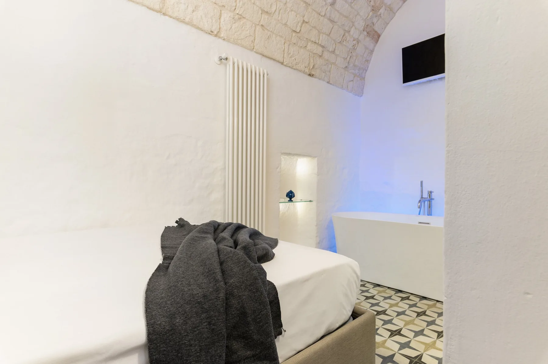 A bedroom with a bed, a freestanding bathtub, and a wall-mounted television.