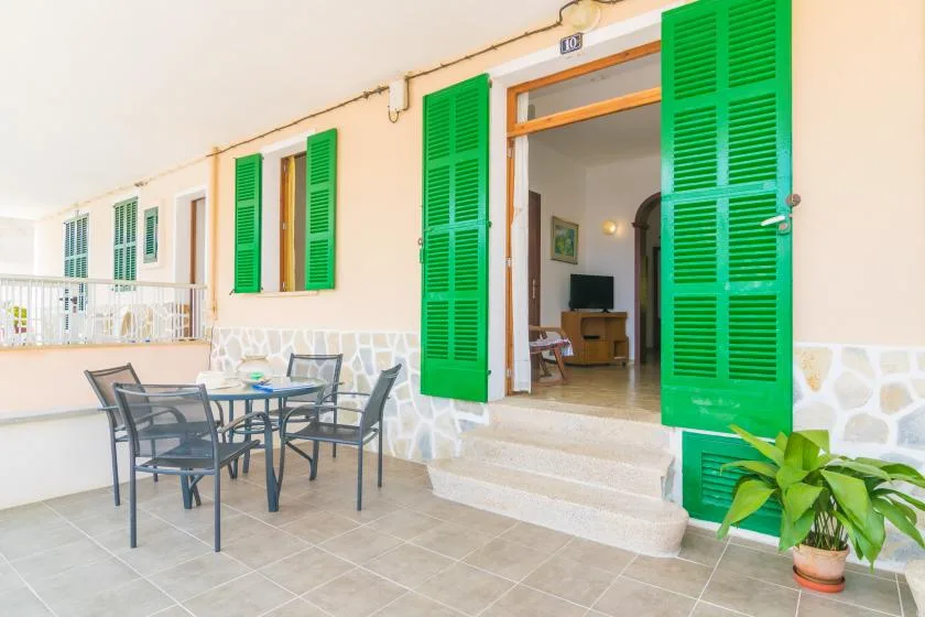 A tiled patio with outdoor seating sits beside an open doorway with green shutters.