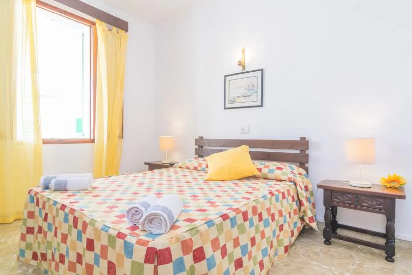 A bedroom with a bed covered in a colorful patchwork quilt and yellow curtains.