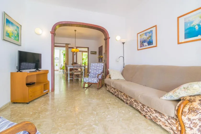 A living room with a long sofa, television, and an arched opening to a dining area.