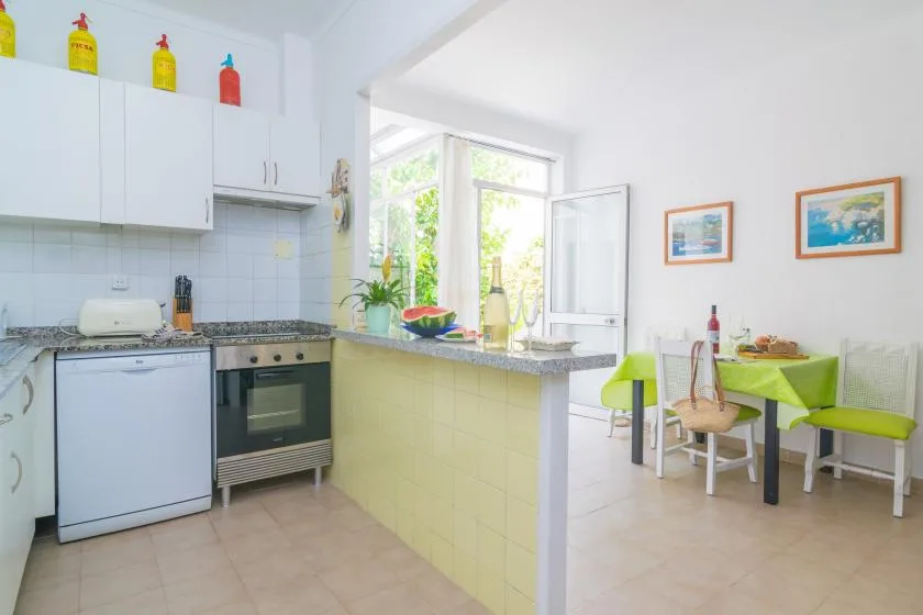A bright kitchen opens onto a dining area with a green tablecloth.