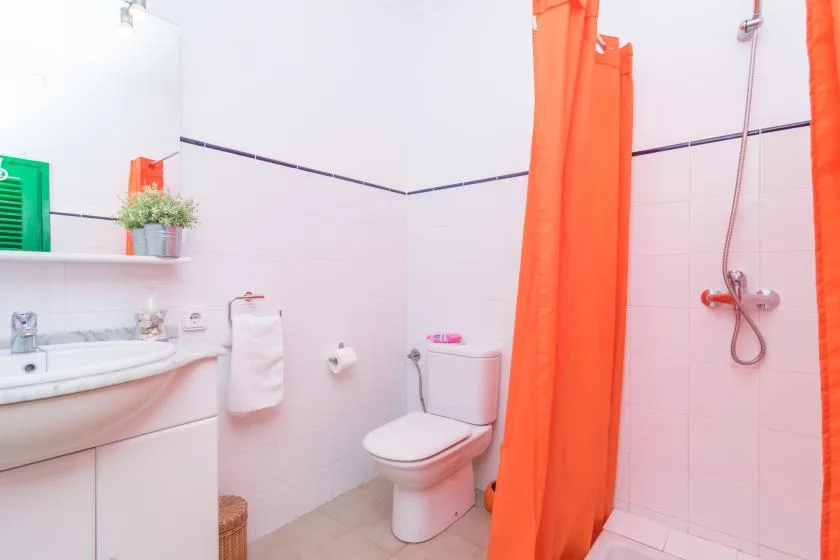 A bathroom with a sink, toilet, and bright orange shower curtain.