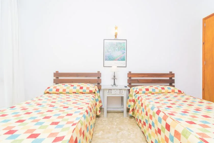 A bright bedroom with two beds covered in colorful patterned bedspreads.