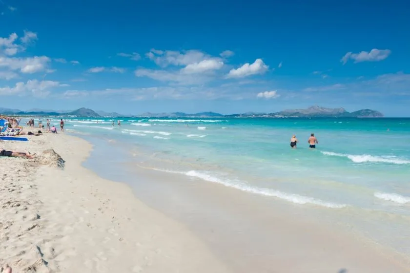A sandy beach meets clear turquoise water beneath a blue sky.
