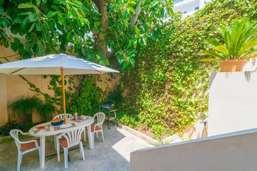 A leafy outdoor patio has a dining table beneath a large umbrella.