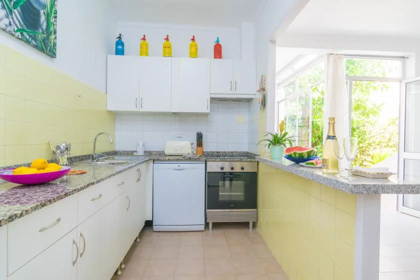 A bright kitchen with white cabinets, tiled walls, and a wide window.