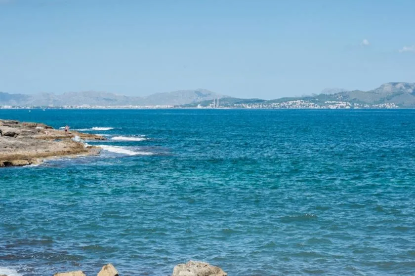 A coastal scene shows blue water, rocky shoreline, and distant mountains.