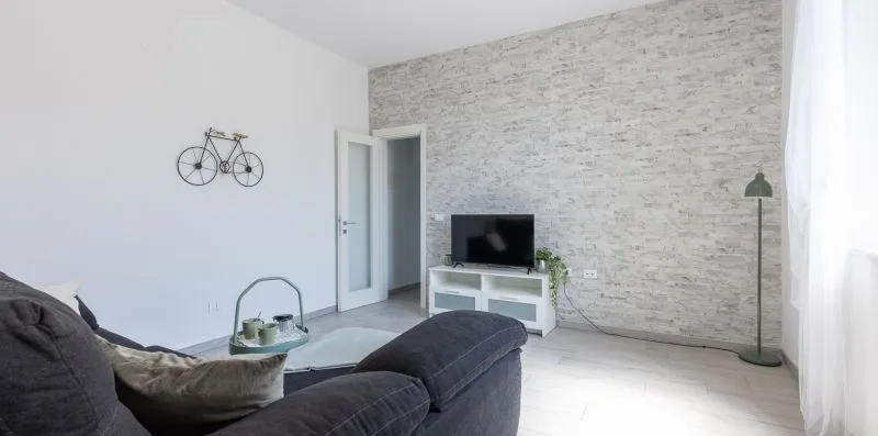 Una sala luminosa con un televisor y asientos junto a una pared texturizada.