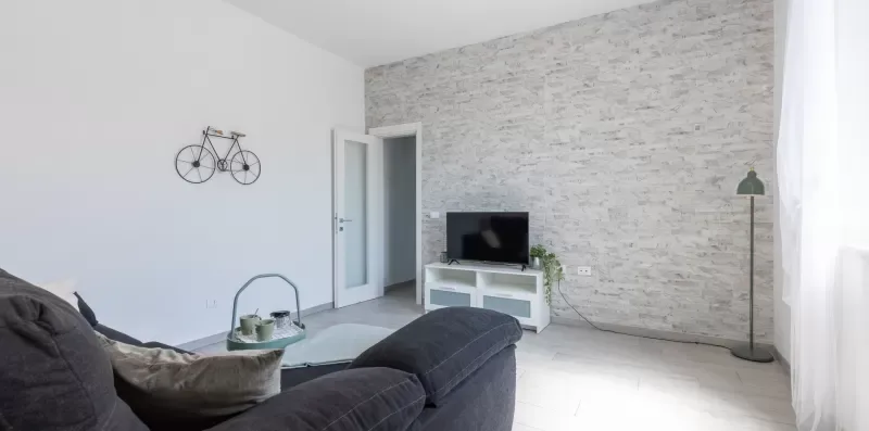 Una sala de estar con sofá, televisor y una pared de ladrillo claro.