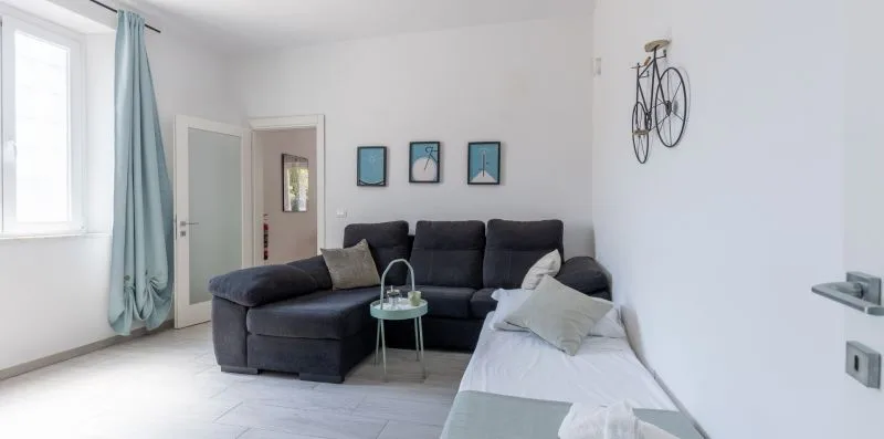 Una sala luminosa con asientos oscuros, una pequeña mesa de vidrio y una cama en primer plano.
