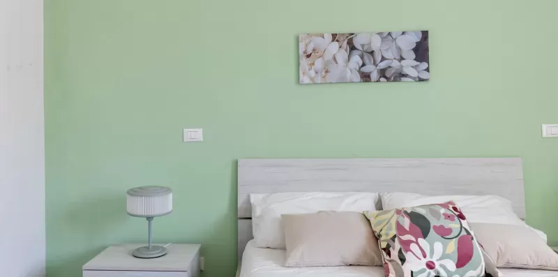 Un dormitorio con una cama junto a una pared verde claro y un cuadro floral.