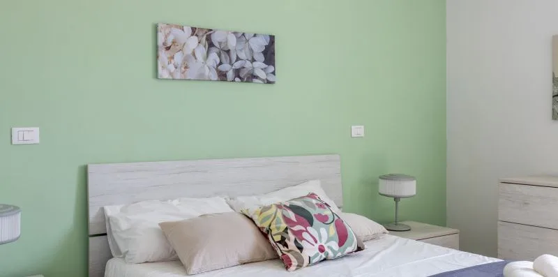 Un dormitorio con una cama, cojines coloridos y paredes verde claro.