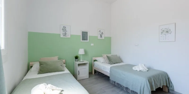Un dormitorio con dos camas, paredes verdes y blancas, y cuadros sencillos.