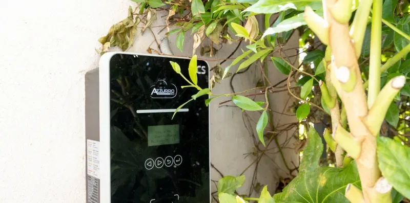 Un panel de control montado en la pared está entre plantas frondosas.
