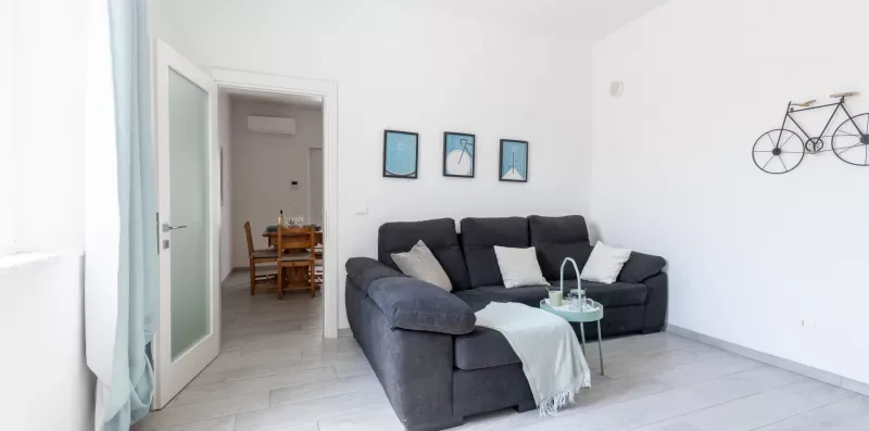 Una sala luminosa con un sofá seccional oscuro y cuadros en la pared.