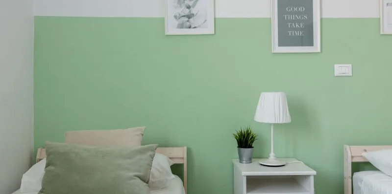 Un dormitorio con paredes verdes, mesitas de noche y cuadros enmarcados.