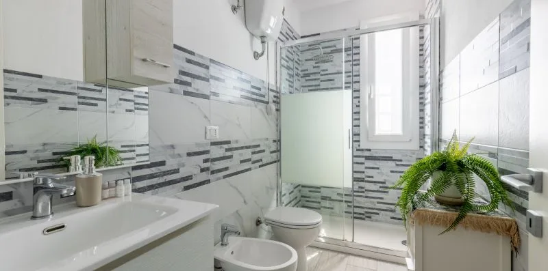 Un baño luminoso con azulejos, lavabo, inodoro y una planta frondosa.