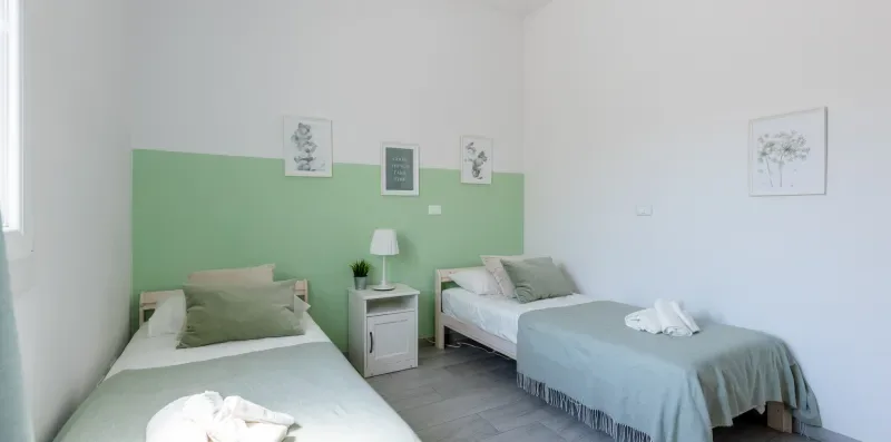 Un dormitorio luminoso con dos camas, detalles verde claro en la pared y cuadros.