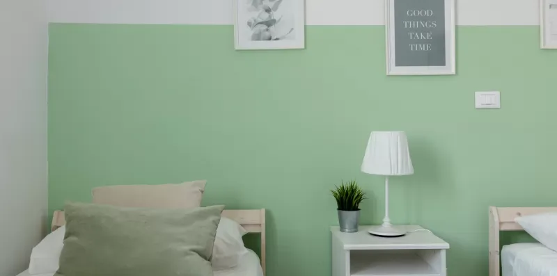 Un dormitorio con camas, una mesa auxiliar y una lámpara frente a una pared verde.