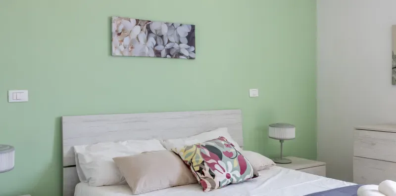 Un dormitorio con una cama, cojines decorativos y un cuadro floral.